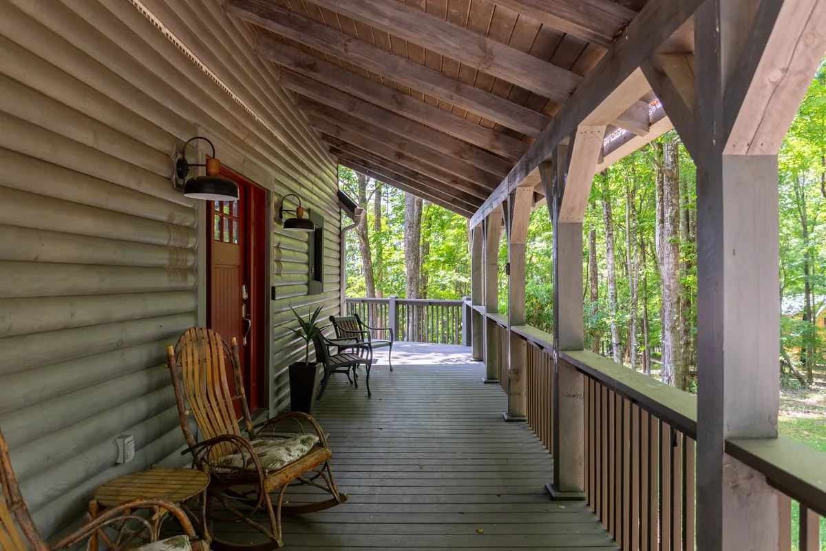 The cozy front porch with rocking chairs, wooden railings, and verdant greenery forms a tranquil setting for guests to unwind, socialize, and take in the natural beauty surrounding the cabin.