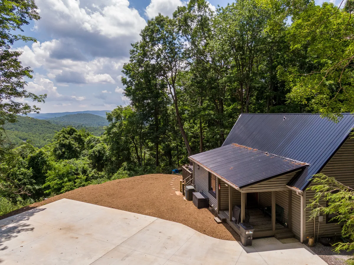 A modern cabin nestled among tall trees, with a wide cleared area in front that opens up to majestic mountain views. The scene emphasizes the cabin’s connection to nature and the inviting outdoor spaces ideal for gatherings and enjoying the High Country environment.