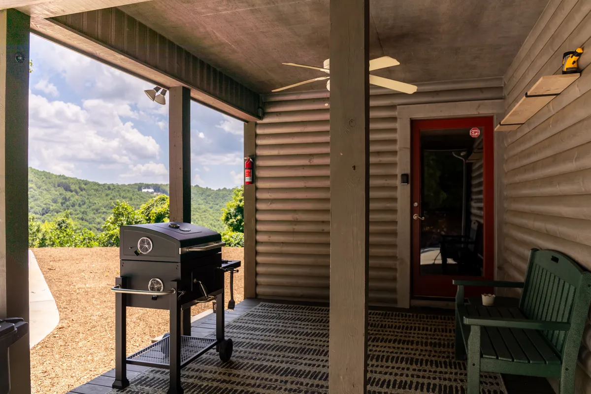 An exterior shot featuring a grill and green chair on a porch with views of the rolling hills. The setup suggests al fresco dining and casual group hangouts, with scenic surroundings enhancing the appeal.