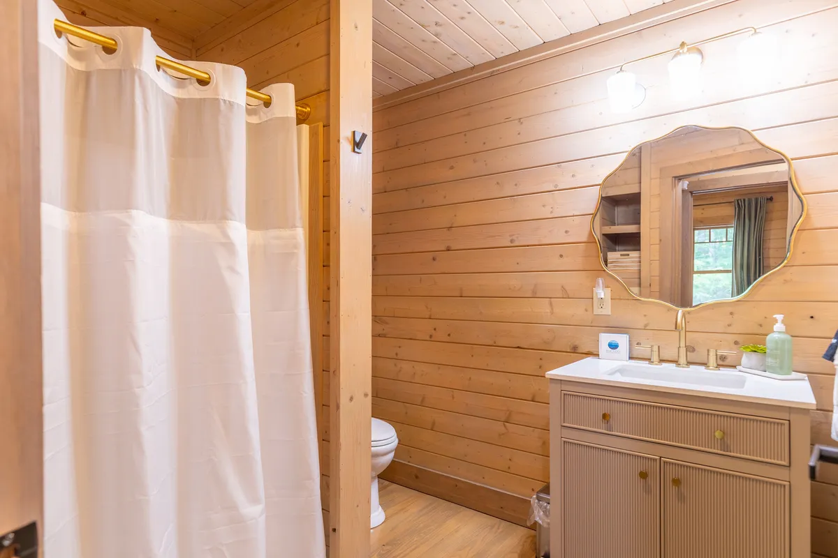 A well-appointed bathroom featuring a shower curtain, a vanity with mirror, and wooden walls that contribute to a cozy, cabin-like feel. Soft lighting adds to the sense of relaxation.