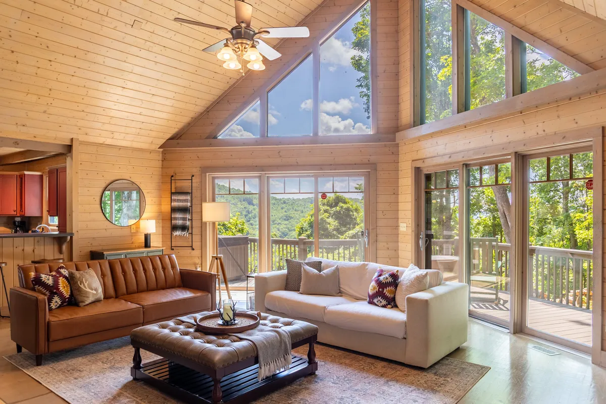Showcasing a stylish brown leather sofa, light fabric sofa, ornate coffee table, and large windows framing mountain scenery, this living area radiates comfort and style. The inviting setup encourages relaxation with a view, seamlessly blending the interior with the natural world outside.