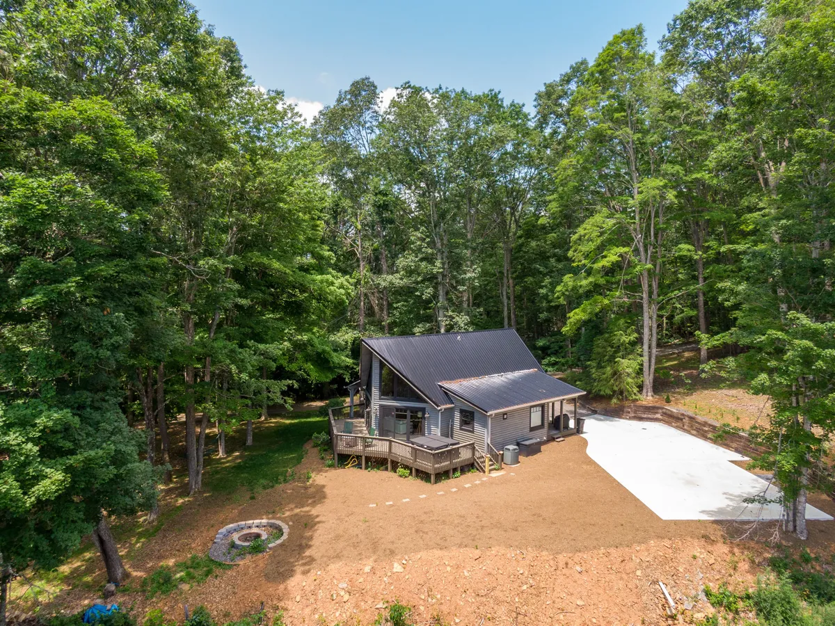 A wide exterior view showcasing the modern house, a spacious deck, and a well-defined fire pit area nestled among trees. The setup highlights the wraparound deck and open yard—spaces perfect for kids or pups to roam while adults relax or host gatherings.