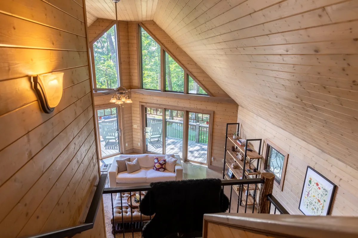 A cozy living area with expansive windows presents sweeping views of the outdoors, inviting natural light inside. The comfortable sofa and rich wood ceiling frame the experience of relaxing while staying connected to the surrounding forest.