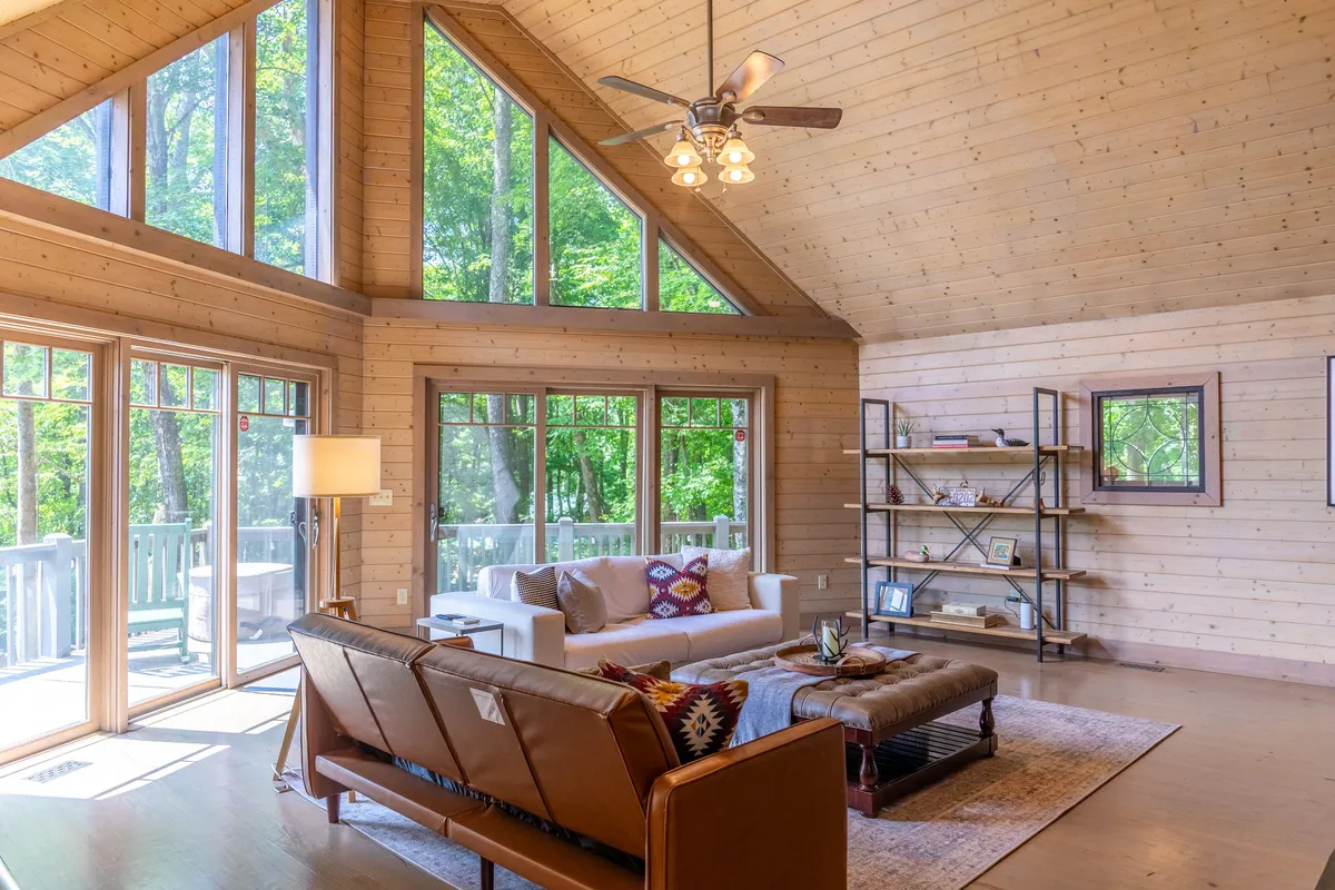 A bright and inviting living area with large windows, a sofa, coffee table, and bookshelf, perfect for enjoying morning coffee with a view or unwinding after outdoor activities. The scene radiates warmth and a connection to the natural setting just outside.