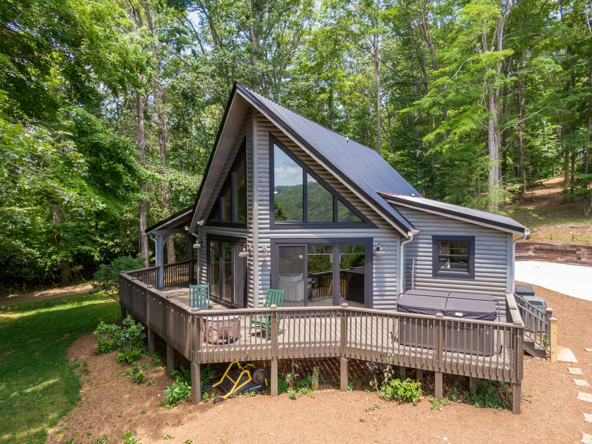 The hero image showcases a charming A-frame cabin nestled among towering trees, with expansive windows and a spacious deck overlooking the mountains. The scene feels tranquil and inviting, hinting at sunset views and outdoor relaxation, with the deck set up for gatherings or peaceful moments with nature.