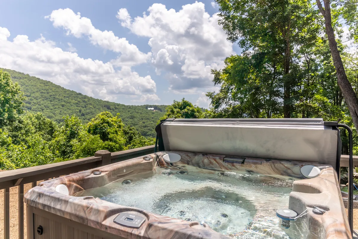 This exterior shot features a bubbling hot tub positioned to capture sweeping mountain vistas, with clouds drifting over the peaks. The tranquil mood and visible hot tub invite thoughts of relaxation and romance, especially at sunset or sunrise, with space for couples to unwind together.