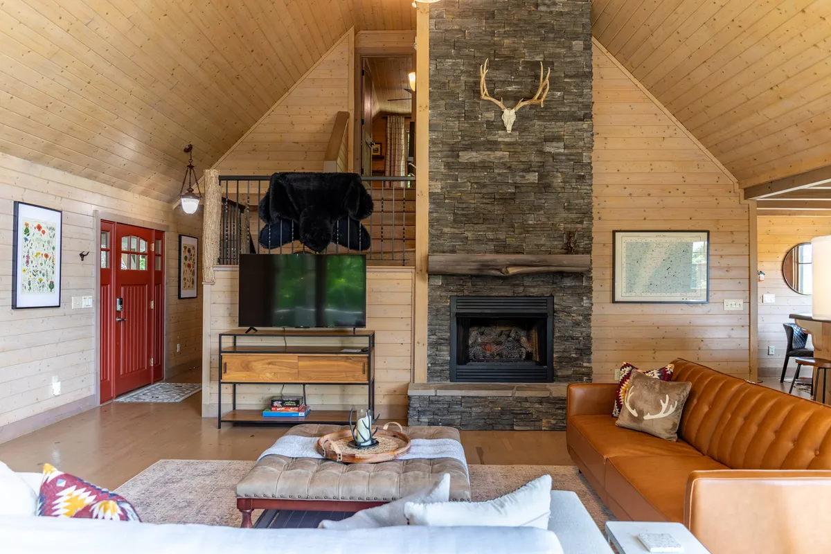 A cozy living area with a stone fireplace, leather sofa, and the signature red front door. The space is designed for relaxation, with warm lighting and comfortable furnishings creating an ideal spot for unwinding by the fire after outdoor explorations.